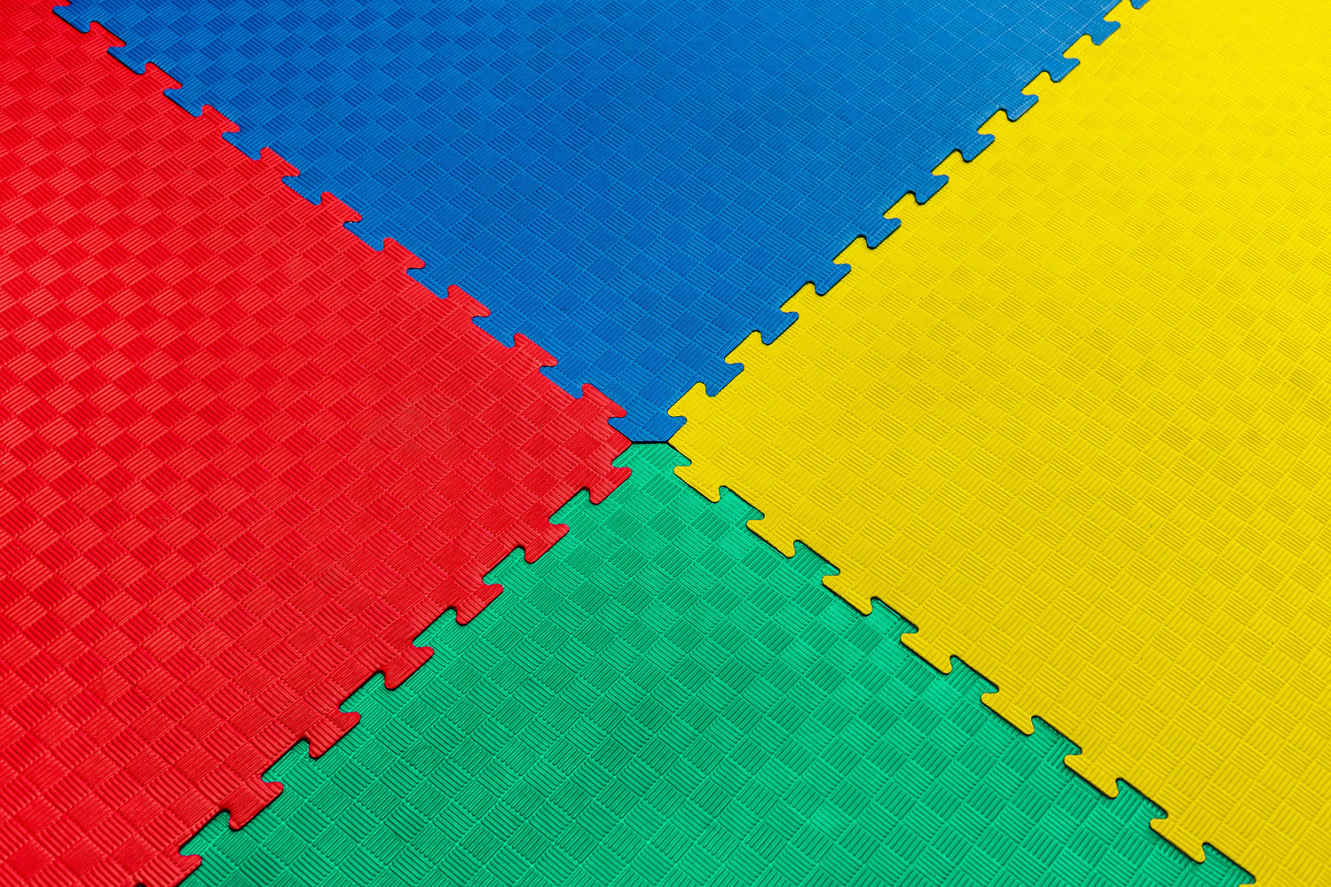 Bunte ineinandergreifende Schaumstoffmatten in Rot, Blau, Gelb und Grün mit strukturierter Oberfläche, die diagonal angeordnet sind.